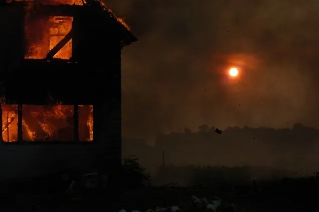 A fire burning in the sky next to a house.