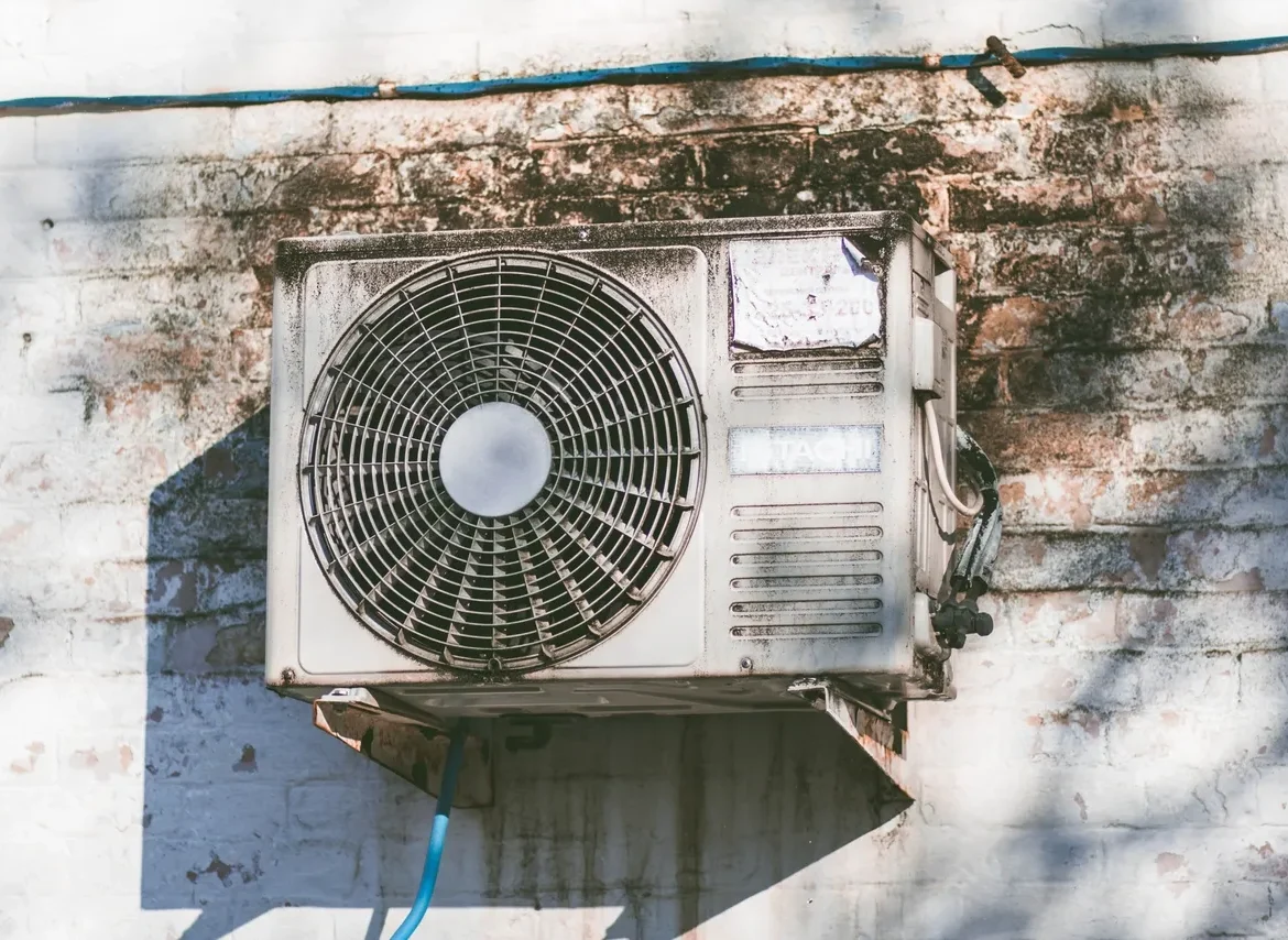 A dirty air conditioner mounted to the side of a building.