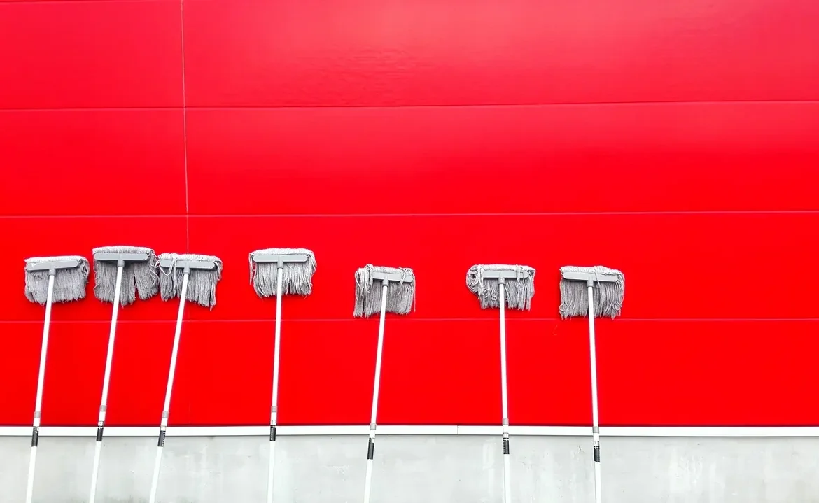 A row of brooms against a red wall.