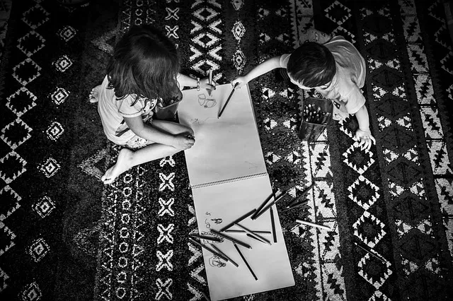 Two children are drawing on a book.