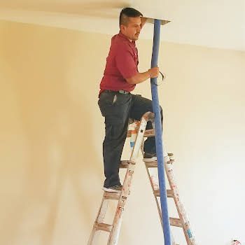 A man on a ladder painting the ceiling of his home.
