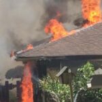 A house that is on fire with smoke coming out of the roof.