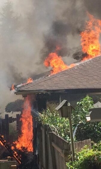 A house that is on fire with smoke coming out of the roof.